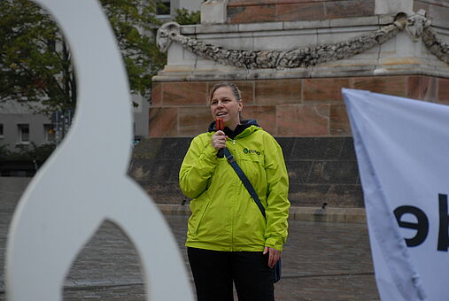 Auf dem Bild ist Franziska Sperfeld vom Unabhängigen Institut für Forschungsfragen zu sehen. Sie hält ein Mikrofon.